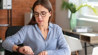 Frau bei der Arbeit, die auf ihre Armbanduhr schaut.