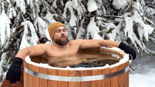 Mann mit Mütze und Handschuhen nimmt im Winter ein Eisbad.