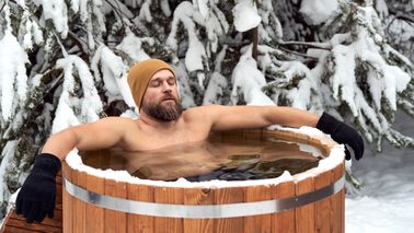 Mann mit Mütze und Handschuhen nimmt im Winter ein Eisbad.