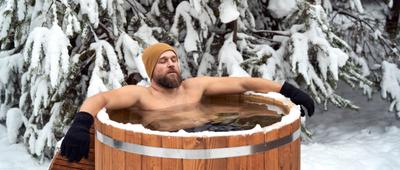 Mann mit Mütze und Handschuhen nimmt im Winter ein Eisbad.