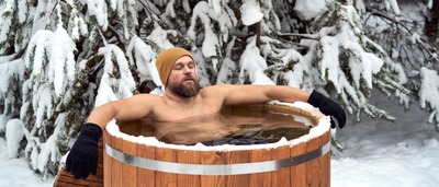 Mann mit Mütze und Handschuhen nimmt im Winter ein Eisbad.