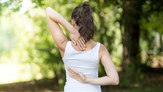 Frau mit Nackenbeschwerden fasst sich an den Nacken.