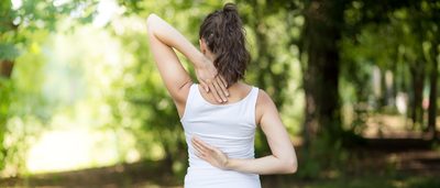 Frau mit Nackenbeschwerden fasst sich an den Nacken.