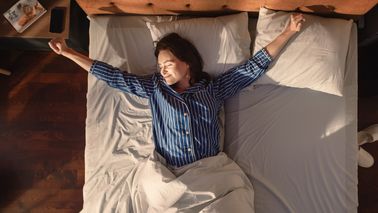 Frau liegt mit offenen Armen auf einem großen Bett und genießt es