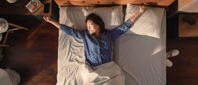 Frau liegt mit offenen Armen auf einem großen Bett und genießt es