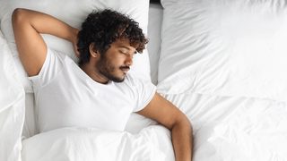 Mann schläft auf dem Rücken in einem Bett.