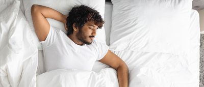 Mann schläft auf dem Rücken in einem Bett.