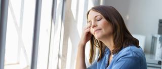 Frau steht mit geschlossenen Augen an einem Fenster.
