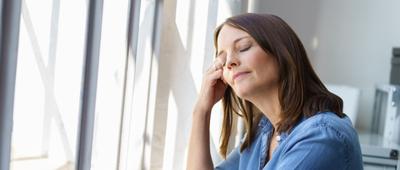 Frau steht mit geschlossenen Augen an einem Fenster.