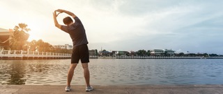 Mann dehnt sich an am Seeufer nach dem Sport
