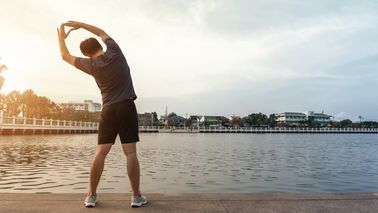 Mann dehnt sich an am Seeufer nach dem Sport