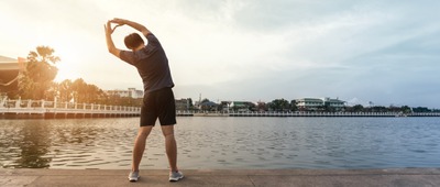 Mann dehnt sich an am Seeufer nach dem Sport