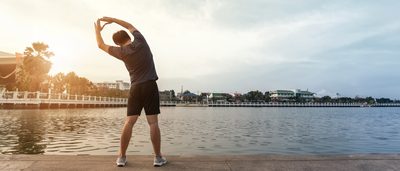 Mann dehnt sich an am Seeufer nach dem Sport