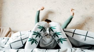 Frau mit Socken mit Cannbismotiv liegt im Bett.