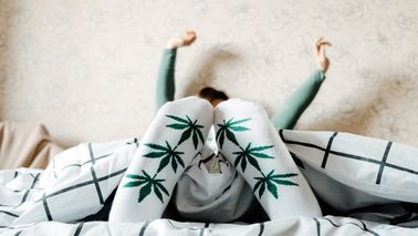 Frau mit Socken mit Cannbismotiv liegt im Bett.