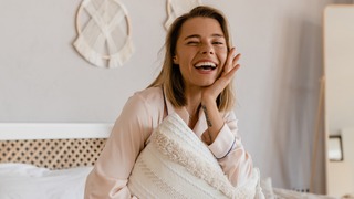 Frau sitzt auf einem Bett und lacht.