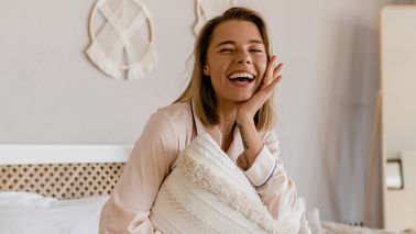 Frau sitzt auf einem Bett und lacht.