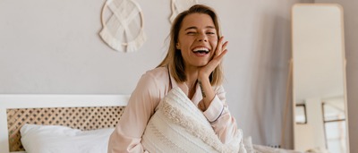 Frau sitzt auf einem Bett und lacht.