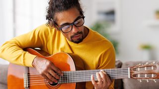 Mann spielt auf einem Stuhl Gitarre.
