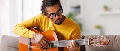 Mann spielt auf einem Stuhl Gitarre.