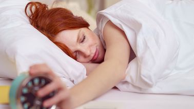 Frau liegt im Bett und stellt ihren Wecker aus.