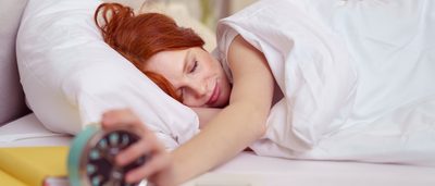 Frau liegt im Bett und stellt ihren Wecker aus.