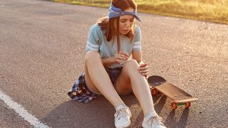 Junge Frau betrachtet einen Bluterguss am Knie nach einem Sturz beim Skateboardfahren
