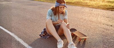 Junge Frau betrachtet einen Bluterguss am Knie nach einem Sturz beim Skateboardfahren