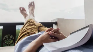 Mann liegt entspannt mit einem Buch auf einem Balkon.