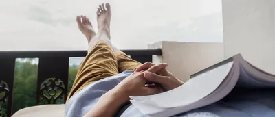 Mann liegt entspannt mit einem Buch auf einem Balkon.