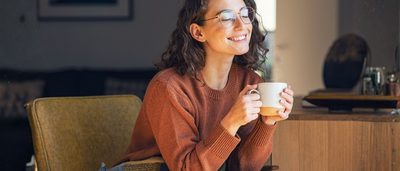 Frau sitzt entspannt mit einer Tasse Tee im Morgenlicht – Symbol für Gelassenheit und Achtsamkeit