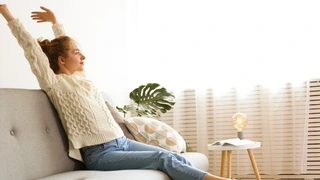 Frau entspannt kurz auf grauem Sofa.