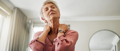 Ältere Frau auf einer Couch fasst sich an den Hals.