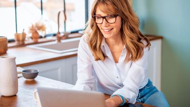 Frau im Homeoffice nutzt Laptop und legt das Smartphone beiseite – sie begegnet digitalem Stress bewusst.