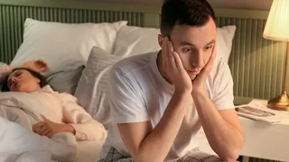 Mann sitzt auf einem Bett und hat Schlafstörungen durch Stress.