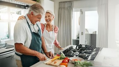 Älteres Paar lacht gemeinsam beim Kochen – Wohlbefinden ohne Sodbrennen