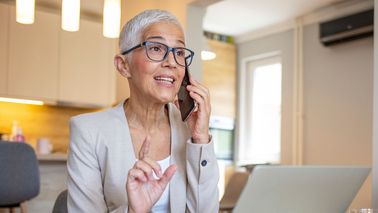 Frau arbeitet im Home-Office, telefoniert und schaut konzentriert auf den Laptop – schwindelfreise Arbeiten.