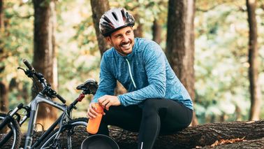 Sportlicher Fahrradfahrer sitzt auf Baumstämmen im Wald.
