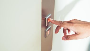 Close-Up von Finger, der auf Knopf eines Aufzugs drückt.