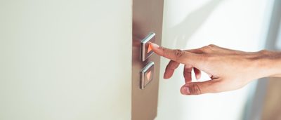 Close-Up von Finger, der auf Knopf eines Aufzugs drückt.