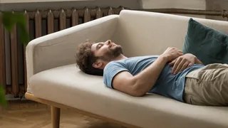 Mann macht eine Entspannungsübung auf dem Sofa. 