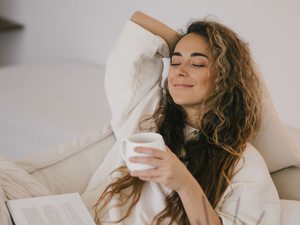 Frau entspannt auf dem Sofa mit Buch und Tee – Stressbewältigung zur Unterstützung des weiblichen Zyklus.