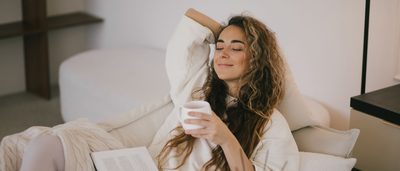 Frau entspannt auf dem Sofa mit Buch und Tee – Stressbewältigung zur Unterstützung des weiblichen Zyklus.
