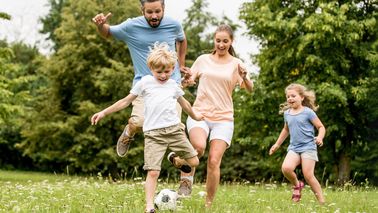 Familie mit zwei kleinen Kindern spielen fröhlich Fußball – gemeinsamer Sommertag in der Natur