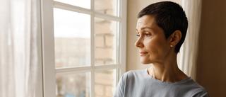 Frau steht am Fenster und schaut nach draußen.