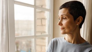 Frau steht am Fenster und schaut nach draußen.