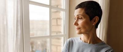 Frau steht am Fenster und schaut nach draußen.