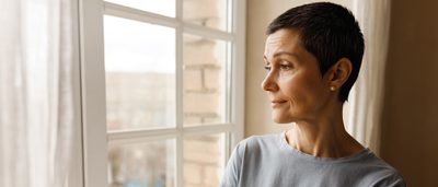 Frau steht am Fenster und schaut nach draußen.