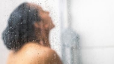 Frau unter der Dusche mit Wasser im Gesicht – belebender Effekt durch morgendliche Wechseldusche