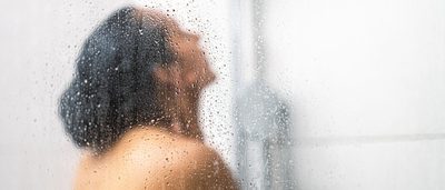 Frau unter der Dusche mit Wasser im Gesicht – belebender Effekt durch morgendliche Wechseldusche